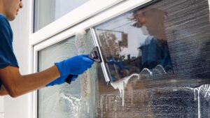 A professional window cleaner running a squeegee over a soaped up window