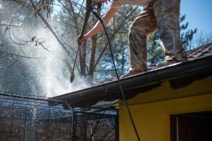 Worker,Standing,On,The,Roof,And,Cleaning,Rain,Gutter,With